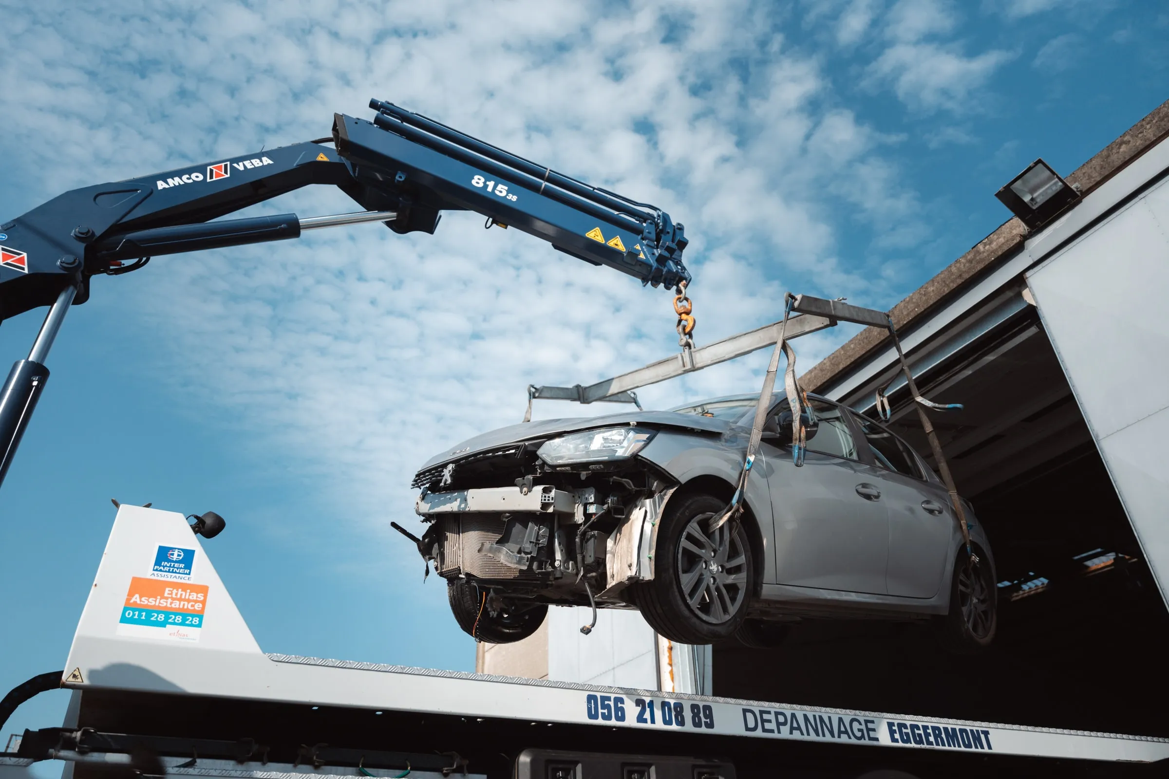 Een beschadigde wagen hangt aan de kraan boven het plateau
