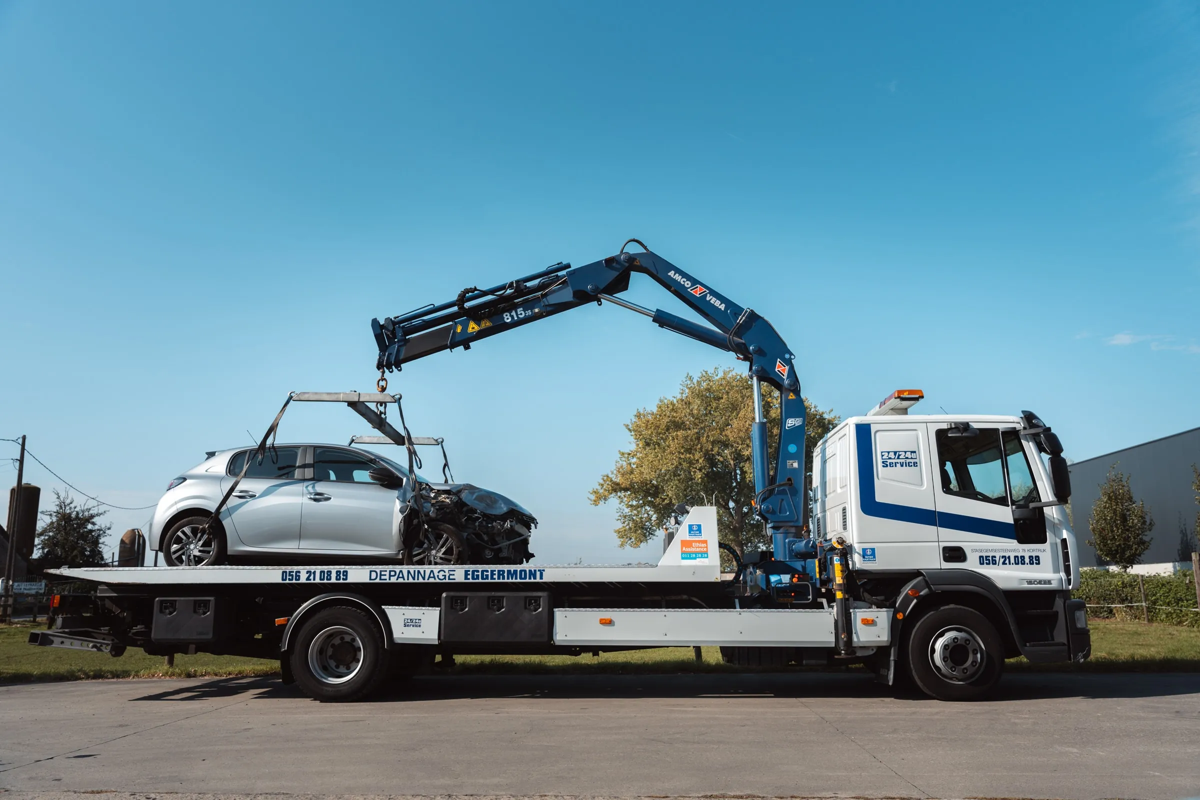 De kraanwagen van opzij, met een beschadigde wagen op het plateau
